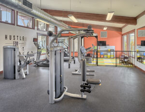 Indoor gym with a variety of workout equipment, large windows, and large mirrors at The Lodge Apartments at Marysville, WA.
