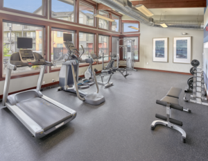 Indoor gym with large windows facing the fenced-in pool at The Lodge Apartments at Marysville, WA.